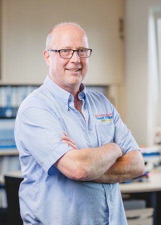 Der Mann in einem hellblauen Hemd strahlt Selbstbewusstsein aus, während er in einem gut beleuchteten Büro posiert.