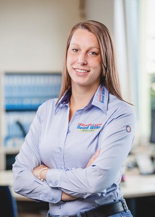 Die Frau mit langen, braunen Haaren trägt ein hellblaues Hemd und strahlt Selbstbewusstsein in einem Büro aus.