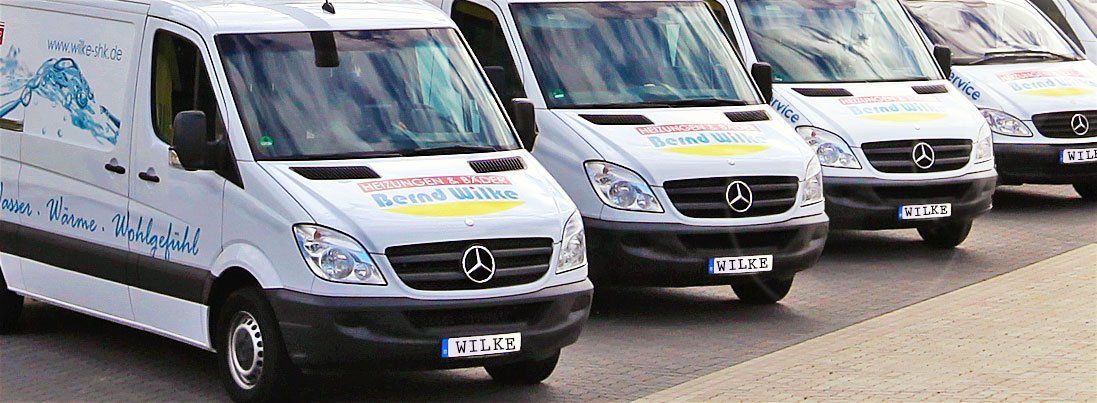 Fünf weiße Lieferwagen mit dem Logo von Bend Wilke stehen ordentlich in einer Reihe auf einem gepflasterten Parkplatz.